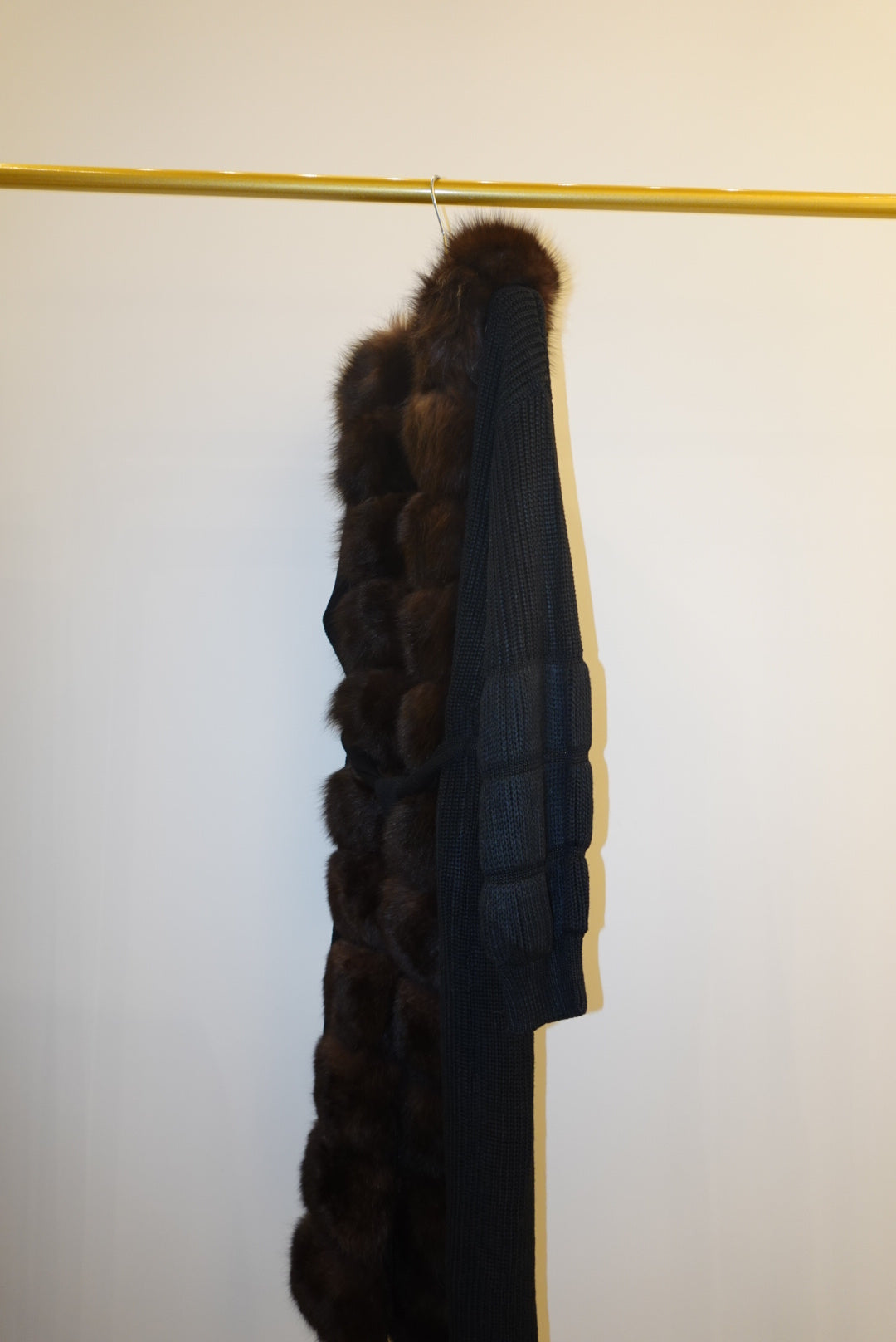 Brown fur-trimmed jackets/cardigan on a rack against a white wall.