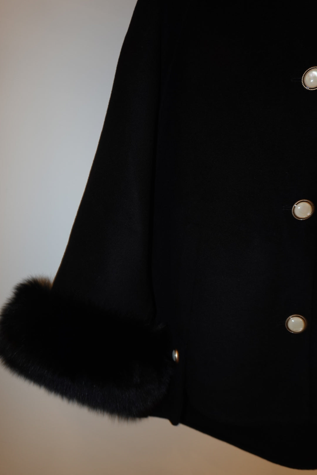 Black coat with fur hood and buttons on a plain background