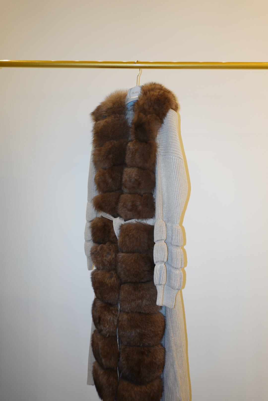Brown fur-trimmed jackets/cardigan on a rack against a white wall.