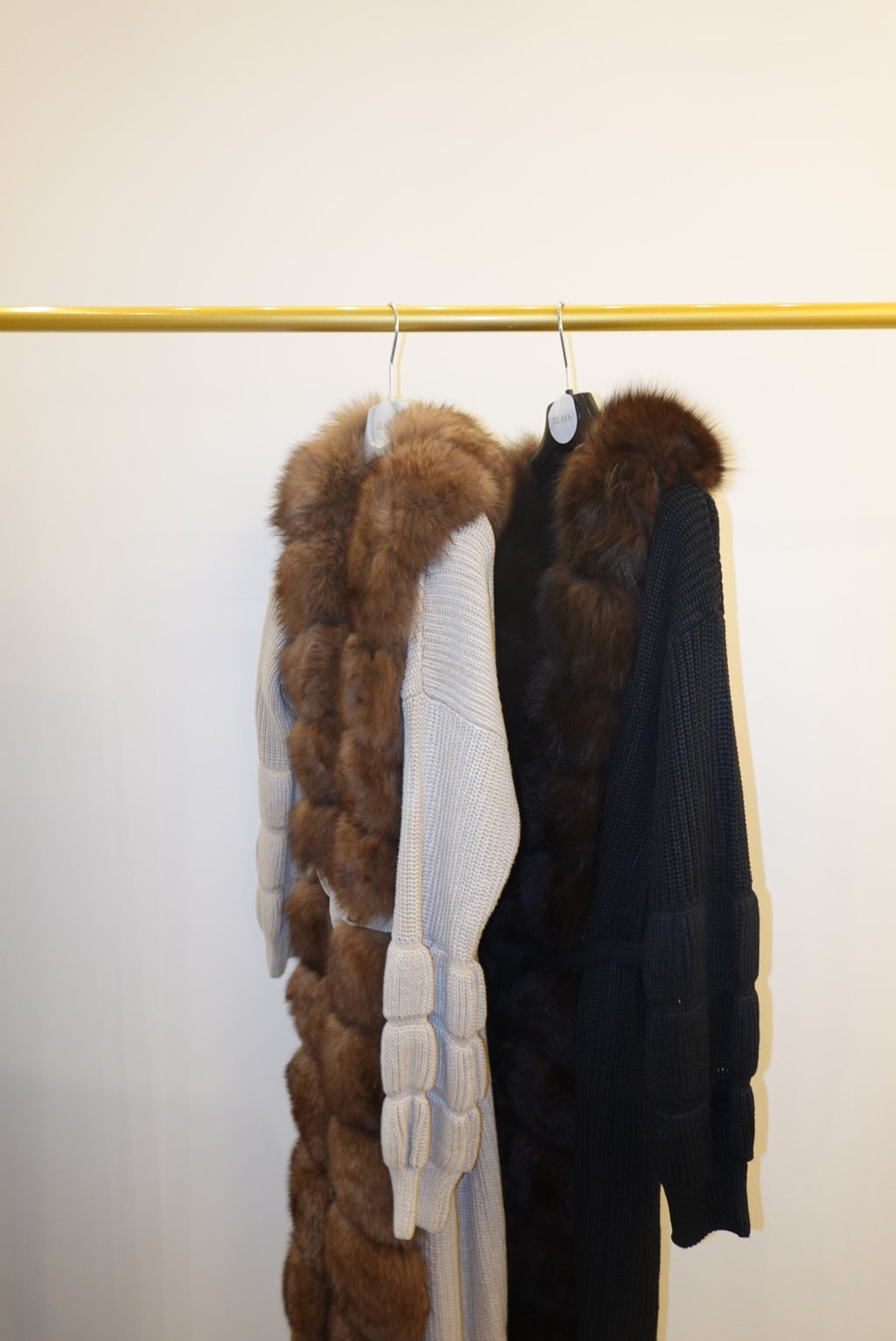 Stack of fur-trimmed jackets/cardigan on a rack against a white wall.