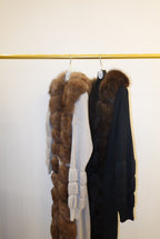 Stack of fur-trimmed jackets/cardigan on a rack against a white wall.