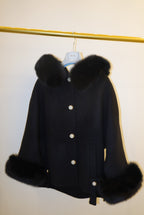 Black coat with fur trim on a stand against a white background