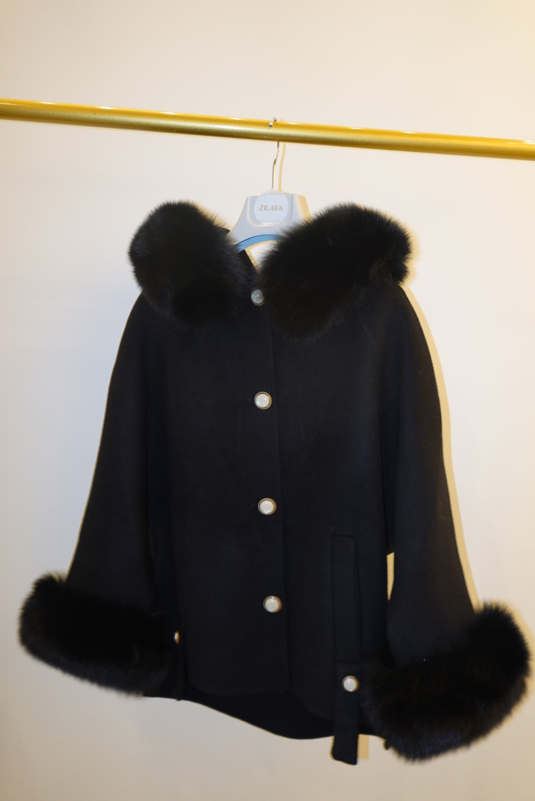 Black coat with fur trim on a stand against a white background
