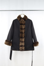 Black coat with fur trim on a hanger against a white background